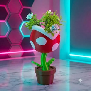 Puede incluir: Una escultura de planta roja con puntos blancos, tallo verde y maceta marrón, que presenta hojas verdes y pequeñas flores azul claro en la parte superior. La planta tiene una forma redondeada con la boca abierta y manchas circulares blancas.