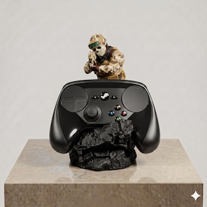 May include: A black video game controller resting on a dark, jagged rock-like base. Positioned behind the controller is a small figurine of a soldier wearing camouflage gear and a skull mask, holding a weapon in a tactical aiming stance.