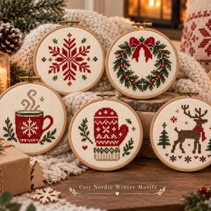 May include: Five circular wooden embroidery hoops containing cross-stitch patterns featuring a red snowflake, a green wreath with a red bow, a red mug with steam, a red patterned mitten, and a brown reindeer with a red scarf on cream fabric.