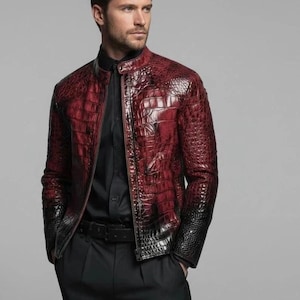 Puede incluir: Una chaqueta de manga larga con un acabado brillante y texturizado que imita la piel de cocodrilo, con un degradado de rojo intenso en la parte superior a negro sólido en el dobladillo. La chaqueta tiene cuello mao, cremallera frontal y mangas.