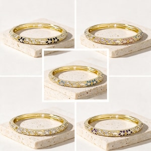 Peut inclure: Une collection de cinq bracelets rigides en métal doré, chacun présentant un motif floral répétitif rempli d'émail de différentes couleurs, dont noir, rose, bleu, blanc et violet, avec de petites pierres claires incrustées au centre.