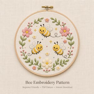 May include: A circular wooden embroidery hoop containing a fabric piece with hand-stitched designs of three yellow and black bees, pink and white flowers, green leaves, and small yellow stars. The text Bee Embroidery Pattern is below the hoop.