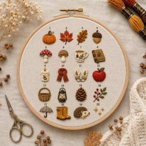 May include: A round wooden embroidery hoop containing a beige fabric panel with twenty numbered autumn-themed embroidered icons, including a pumpkin, maple leaf, oak leaf, acorn, mushroom, tea cup, book, candle, scarf, mittens, apple, basket, lantern, pinecone, berries, umbrella, boots, hedgehog, and stars.
