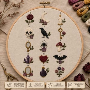 Puede incluir: Un bastidor de bordado redondo de madera que contiene un panel de tela beige con quince motivos bordados numerados que incluyen una rosa, luna creciente, vela, calavera, cuervo, llave, espejo, araña, seta, cristales, corazón, murciélago, marco, poción y flores.