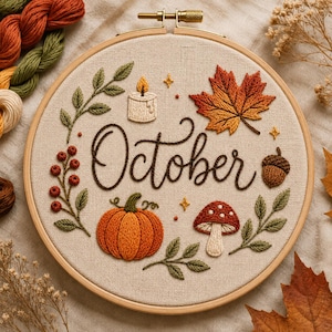 Puede incluir: Un bastidor de bordado con tela beige que muestra la palabra October bordada en cursiva marrón oscuro. El diseño incluye una vela encendida, una hoja de arce naranja vibrante, una bellota marrón, una calabaza, un hongo rojo y ramas verdes.