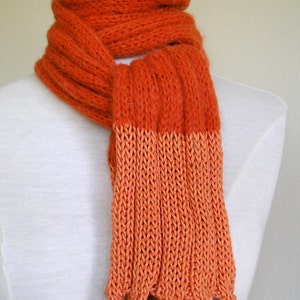 May include: A long, orange knitted scarf with a textured pattern. The scarf is folded in half and draped over a white mannequin.