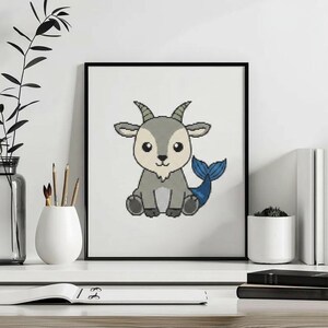 May include: A framed cross-stitch pattern featuring a gray goat with a blue fish tail. The goat has large black eyes, small horns, and a light-colored belly. The design is rendered in a pixelated style against a plain white background within a thin black frame.
