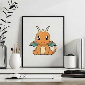 Puede incluir: Una impresión de arte píxel enmarcada que muestra una pequeña criatura dragón naranja con vientre color crema, alas verde azulado y una llama en la punta de la cola. La criatura tiene ojos grandes, dos cuernos pequeños y está sentada.