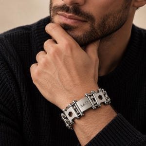 May include: A silver-toned metal link bracelet featuring a mechanical design with hexagonal cutouts and a central rectangular plate engraved with the letters A&O. The bracelet is constructed from interconnected segments resembling industrial hardware components.