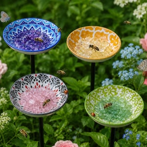 Può includere: Quattro picchetti da giardino decorativi con ciotole poco profonde dai motivi complessi in blu, giallo, bianco e nero, e verde. Ogni ciotola è riempita con piccoli sassolini di vetro traslucido in colori coordinati, che attirano api e farfalle.