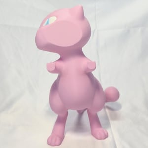 May include: A light pink figurine of a bipedal creature with a rounded head, pointed ears, small arms, and a long tail. The creature features large, almond-shaped eyes with light blue irises and white sclera, standing in an upright position.