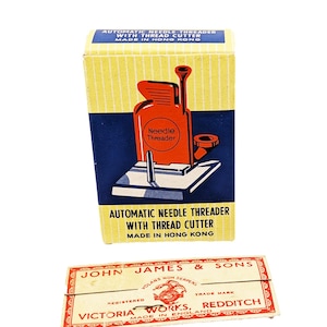 May include: A rectangular yellow and blue box labeled Automatic Needle Threader with Thread Cutter Made in Hong Kong, paired with a rectangular cream-colored paper packet labeled John James & Sons Victoria Works Redditch Made in England.