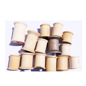 May include: A collection of wooden spools in various shades of light brown and one dark brown spool. The spools are cylindrical with flared edges, and some have visible red thread remnants.