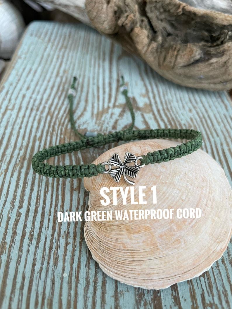 May include: Dark green waterproof cord bracelet with a silver-colored four-leaf clover charm. The bracelet is displayed on a seashell. Text on the image reads "STYLE 1 DARK GREEN WATERPROOF CORD."