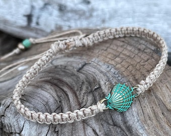 May include: A macrame bracelet with a beige woven band and a turquoise seashell charm. The bracelet is adjustable and features a small green bead. The charm is a detailed, metallic seashell design.