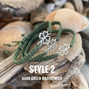 May include: Dark green waterproof bracelets with silver clover charms. The bracelets are made of woven cord and are displayed on driftwood with seashells in the background. The text "STYLE 2 DARK GREEN WATERPROOF" is visible.