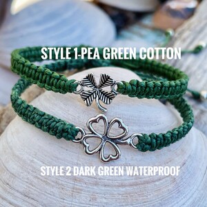 May include: Two green macrame bracelets with silver clover charms. One is pea green cotton, the other is dark green waterproof. The bracelets are displayed on a seashell. Text on the image reads "STYLE 1-PEA GREEN COTTON" and "STYLE 2 DARK GREEN WATERPROOF."
