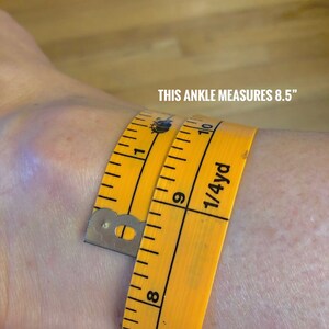 May include: A yellow measuring tape wrapped around an ankle, showing a measurement of 8.5 inches. The text "THIS ANKLE MEASURES 8.5" is visible in white.