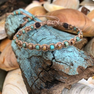 May include: A handmade macrame bracelet with turquoise and brown beads. The bracelet is made of natural-colored cord and features a sliding knot closure. The beads are interspersed with darker brown wooden beads. The bracelet rests on a piece of weathered, blue-painted wood.