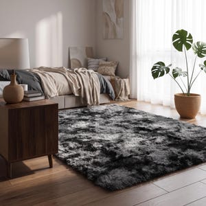 Peut inclure: Un tapis rectangulaire doté d'un poil épais et hirsute avec un motif dégradé passant du noir charbon profond aux nuances de gris plus claires, créant un aspect texturé et multi-tonal sur toute la surface du tapis.