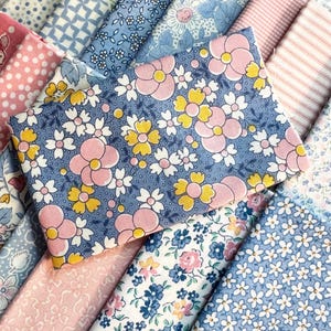 May include: A collection of folded fabric swatches featuring various floral and geometric patterns in shades of blue, pink, and yellow. The prints include small white daisies, larger pink and yellow blossoms, pink stripes, and blue polka dots.