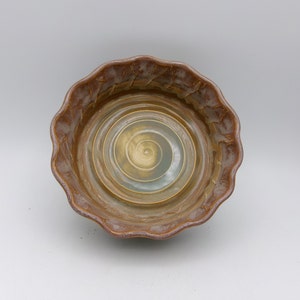 May include: A brown ceramic bowl with a scalloped rim and a swirling pattern in the center. The bowl is glazed in a light brown color with a hint of green.