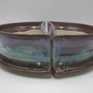 Könnte beinhalten: Ein zweiteiliger Keramik-Pflanztopf mit dunkelbraunem Rand und blau-grüner Glasur. Der Pflanztopf steht auf einer passenden Untertasse. Der Innenraum ist hellbeige. Die Gesamtform ist oval.