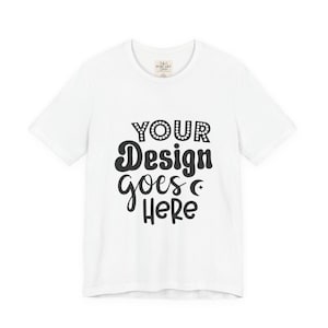Puede incluir: Una camiseta blanca de manga corta con texto negro en la parte delantera que dice YOUR Design goes HERE, junto a un pequeño icono de estrella al lado de la palabra goes. La prenda tiene cuello redondo y una etiqueta de marca en el interior.