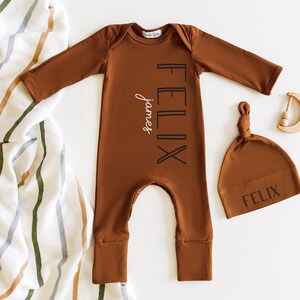 May include: A brown baby onesie with the name "Felix James" printed on the front. A matching brown beanie with the name "Felix" is also included.