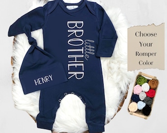 May include: Navy blue baby romper with long sleeves and the text "little brother" in white. The romper is paired with a matching navy blue hat with the name "HENRY" embroidered in white.