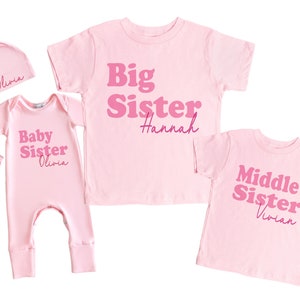 May include: Pink baby onesie with the text "Baby Sister Olivia" in pink, a pink headband, a pink hat with the text "Olivia" in pink, a pink t-shirt with the text "Big Sister Hannah" in pink, and a pink t-shirt with the text "Middle Sister Vivian" in pink.