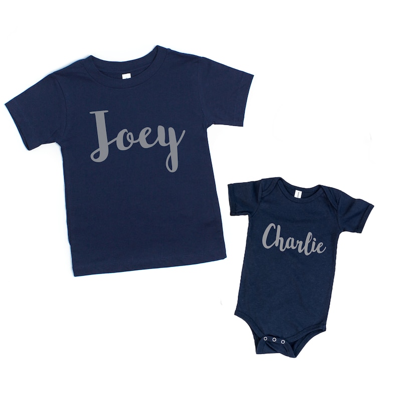 Może przedstawiać: Dwie koszulki w kolorze granatowym z nadrukiem imion "Joey" i "Charlie" w kolorze szarym z przodu.