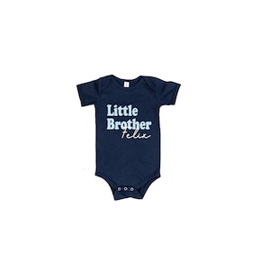 May include: A navy blue baby onesie with the text "Little Brother Felix" in light blue and white.