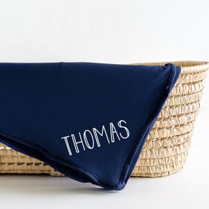 May include: A navy blue baby blanket with the name "THOMAS" embroidered in white.
