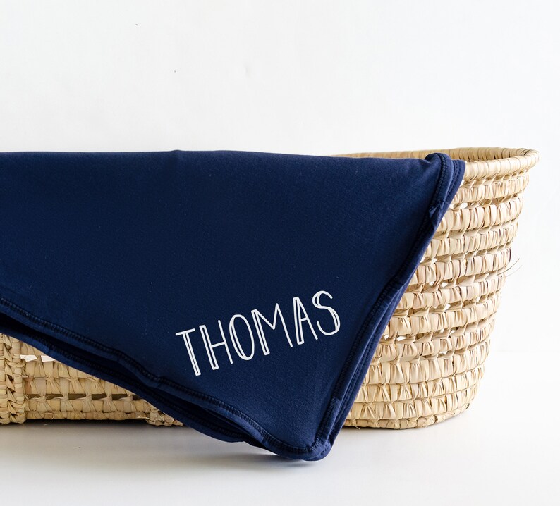 May include: A navy blue baby blanket with the name "THOMAS" embroidered in white.