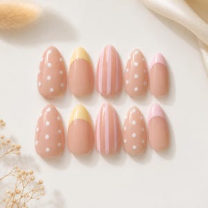 Puede incluir: Un conjunto de diez uñas postizas en forma de almendra con acabado brillante. Los diseños incluyen una base nude con puntos blancos, una base nude con puntas amarillas, una base nude con rayas verticales rosas y puntas rosa claro sólidas.
