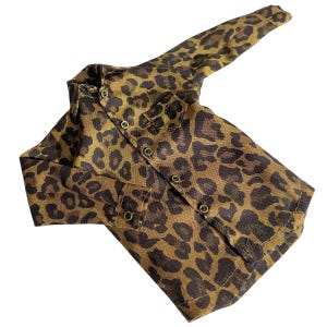 May include: A long-sleeved button-down shirt featuring a brown and black leopard print pattern. The garment includes a pointed collar, a single chest pocket on the left side, and small metallic buttons running down the front placket and cuffs.