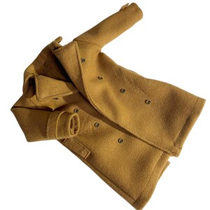 May include: A mustard yellow double-breasted coat featuring a wide notched lapel, long sleeves with buttoned cuffs, and two rows of dark circular buttons down the front. The garment has a textured finish and a structured collar design.