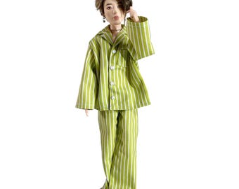 May include: A doll with short brown hair wearing a lime green and white vertical striped pajama set. The long-sleeved button-down top features a collar and a chest pocket, paired with matching long trousers. The doll has a neutral expression.