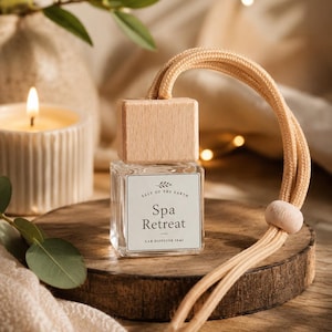 May include: A clear glass car diffuser bottle with a light wood cap and a beige hanging cord. The white label features the text Salt of the Earth, Spa Retreat, and Car Diffuser 10ml. The bottle is square-shaped with a small wooden bead on the cord.