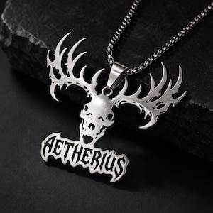 May include: A silver-toned metal pendant necklace featuring a stylised skull with large, branching antlers extending upwards. Below the skull, the word AETHERIUS is engraved in a bold, gothic-inspired font. The pendant hangs from a thin metal chain.
