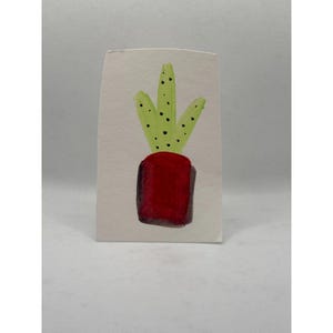 May include: A rectangular piece of off-white paper featuring a watercolor painting of a potted plant. The plant has three light green, upright, pointed leaves with small black dots, set inside a solid, deep red, rectangular-shaped pot.