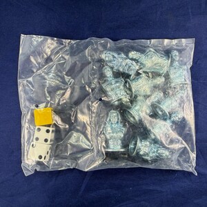 May include: A clear plastic bag contains a set of game pieces. Inside are several silver-colored bust figurines and two dice. One die is white with black dots, and the other is yellow.