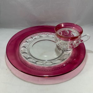 May include: A pink glass dessert plate with a clear glass center and a clear glass cup with a pink rim.