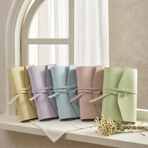 Puede incluir: Cinco diarios rectangulares con cubiertas lisas en amarillo pastel, lavanda, azul claro, rosa empolvado y verde salvia. Cada diario cuenta con un cierre de lazo envolvente hecho del mismo material, que asegura la cubierta al lomo.