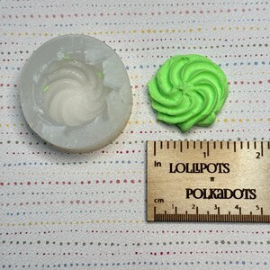 以下が含まれることがあります： シリコンモールドと緑色の渦巻き状のオブジェクト。モールドは円形で、渦巻きのデザインが含まれています。緑色のオブジェクトは渦巻きの形で、おそらく装飾的な要素です。「LOLLIPOPS」と「POLKADOTS」の文字が入った木製の定規も存在します。