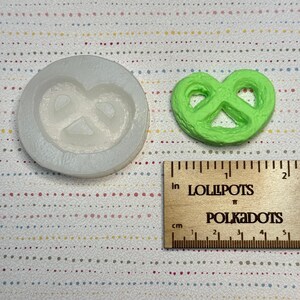 以下が含まれることがあります： 明るい色のシリコンプレッツェル型と、明るい緑色のプレッツェル型のアイテム。 木製の定規にはインチとセンチメートルが表示されています。 定規には「LOLLIPOPS」と「POLKADOTS」の文字が印刷されています。