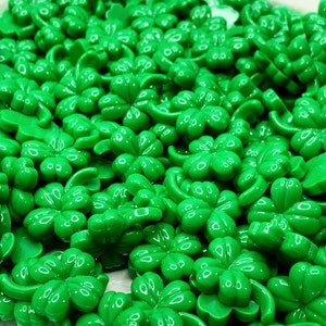 May include: A bowl filled with green four-leaf clover charms. The charms are made of plastic and have a shiny finish.