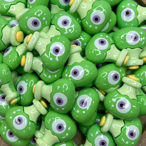 May include: A collection of green glass bottle charms with a single purple eye on each. The charms are in the shape of a bottle with a cork top.