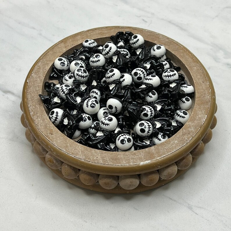 May include: A bowl filled with black and white skull-shaped buttons. The buttons are small and have a glossy finish.